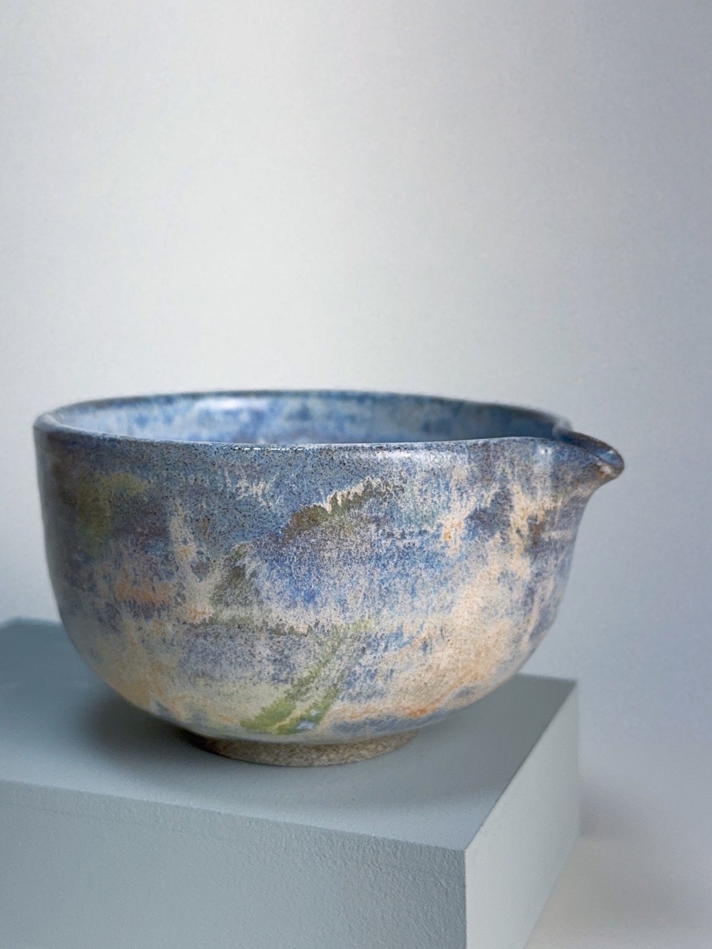 Ceramic bowl with blue and brown glaze on a white pedestal against a light white background
